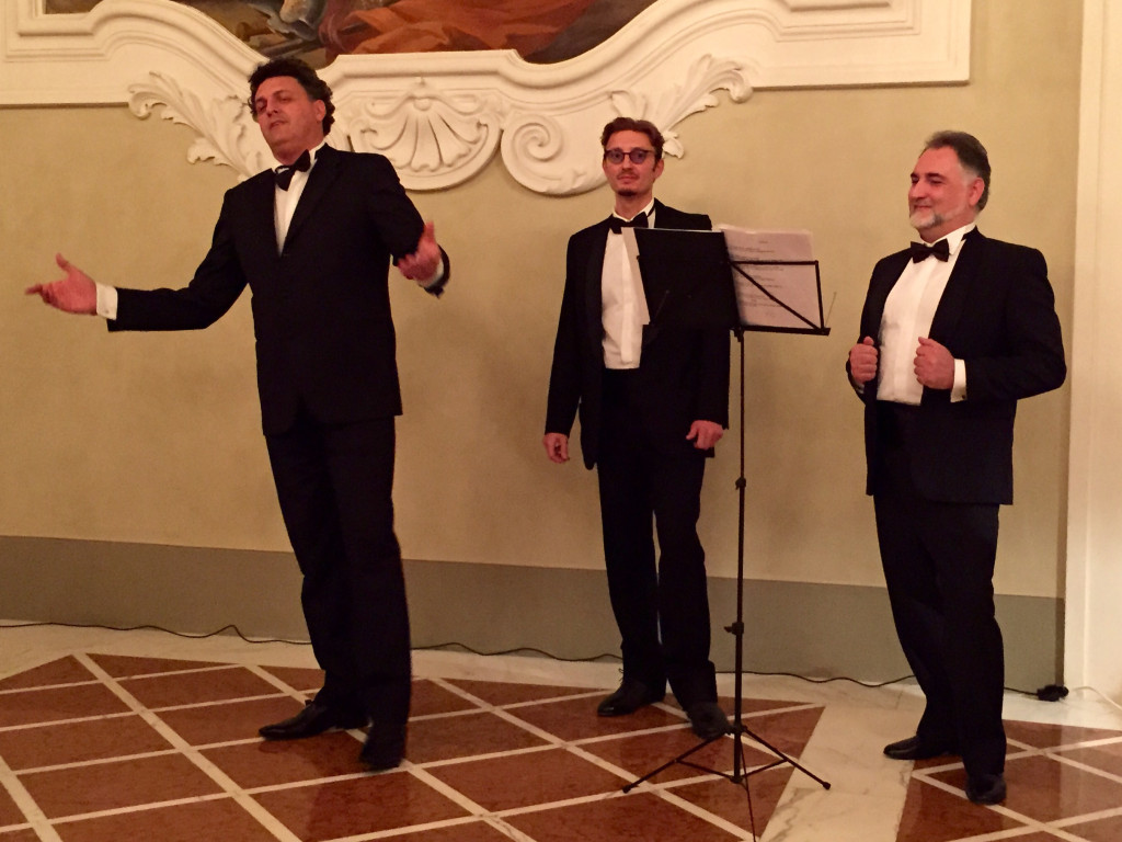 Three men in suits and ties singing on a stage.
