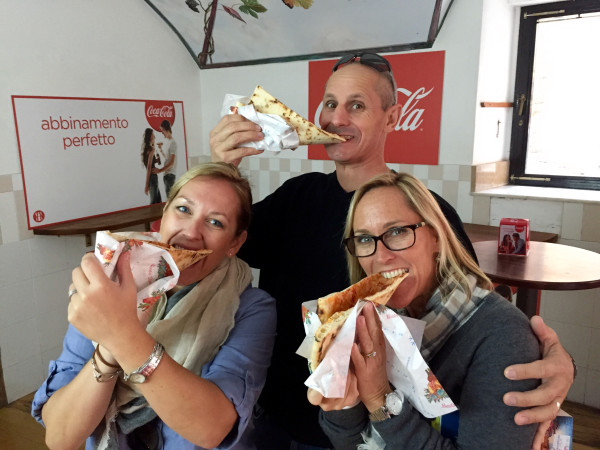 Three people eating a large sandwich in front of coca cola.